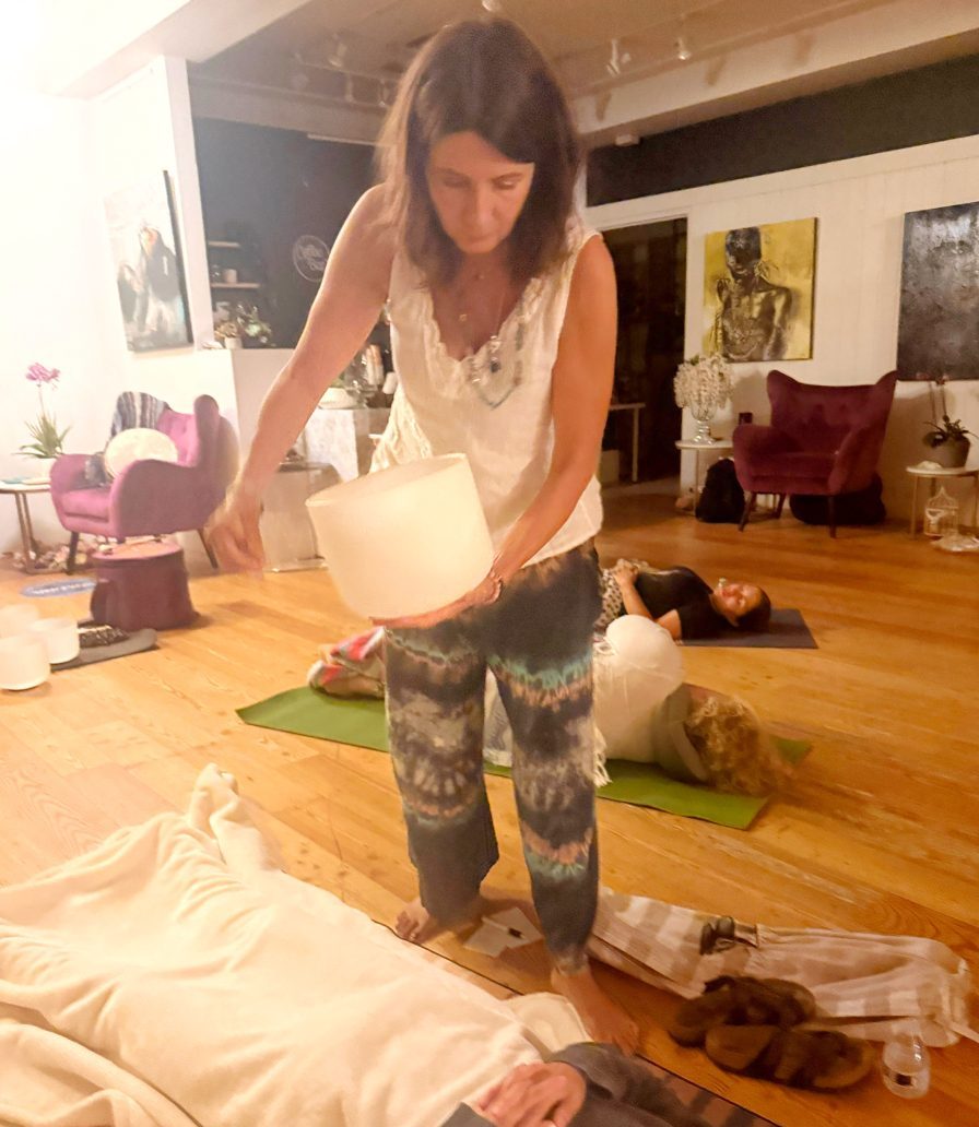 Sophie Anne holding a crystal singing bowl over a guest during a sound bath