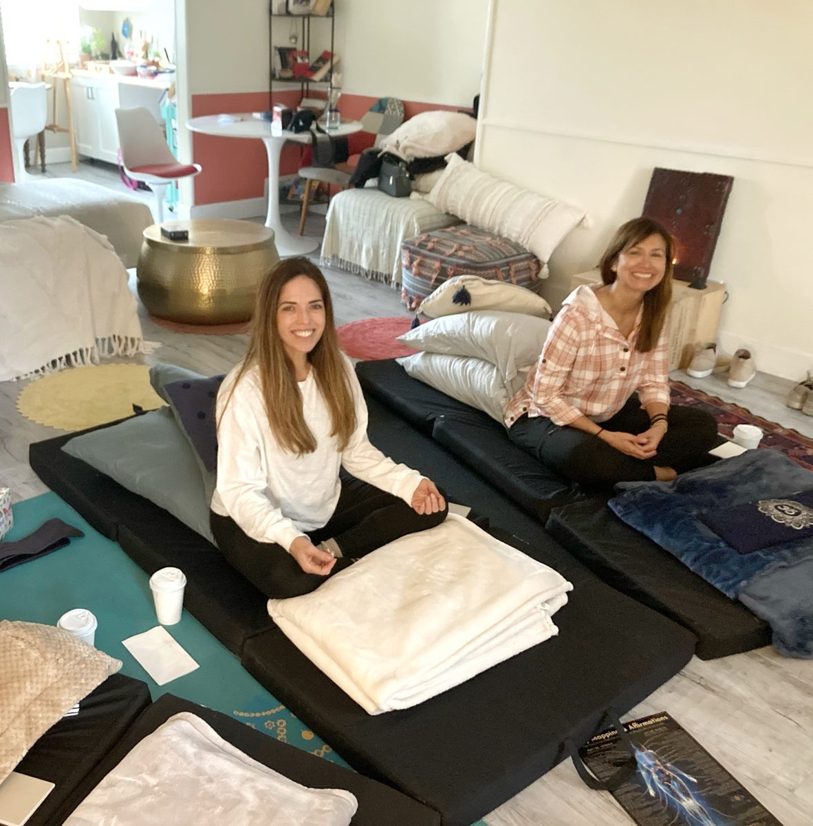 Two smiling participants seated on cushions in the Soul Oasis workshop space